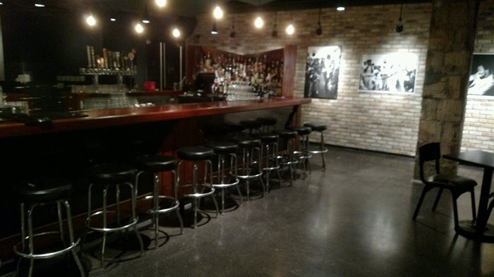 concrete floor with dark wood bar, stools, and brick walls.